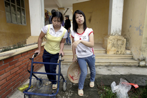 Photo of two young women leaving a building. One is using a walker.