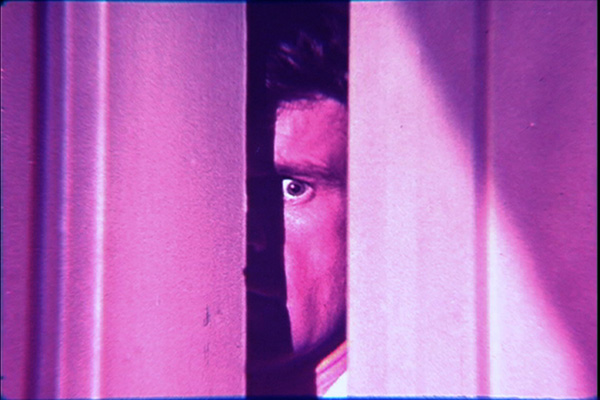 A shot from the film in which a man is peering into a room through a slightly opened door.