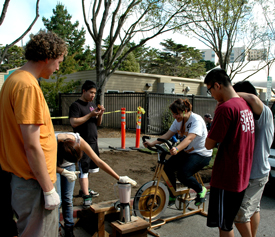 A photo of students making a smoothie using a blender powered by a stationary bicycle