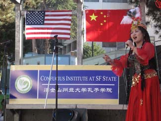 A photo of a Chinese singer in front of the American and Chinese flags and a Confucius Institute SFSU banner.