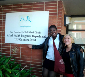 Students Kayla Daniels and Vaneka Reed in front of a sign for the San Francisco Unified School District's School Health Programs Department.  