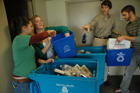 A photo of four students placing bottles in a recycling bin.