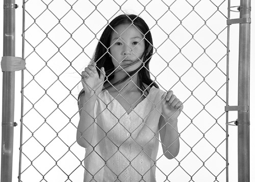 Photo of a young female dancer looking out from behind a chain link fence
