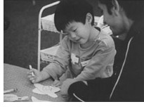 Photo of a young boy working on a project alongside a child center aide