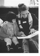 Photo of a young girl reading a book with a child center aide
