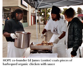 Photo of HOPE co-founder Ed James coating pieces of barbequed organic chicken with sauce