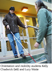 Photo of blindfolded orientation and mobility student Kelly Chadwick learning how to navigate using a white cane with the assistance of classmate Lucy Waite  