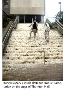 Photo of students Mark Ciotola and Roque Baron-Jordan standing amid cascading water on the steps of Thornton Hall 