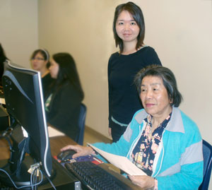 Photograph of older student Du-Mei Tan sitting at a computer with SHINE coach Naoko Takano standing beside her