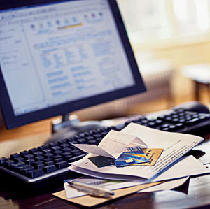 Photo of a computer with a pile of papers and credits cards near the keyboard.