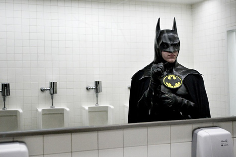 Photo of a man adjusting his Batman costume in the mirror of a men's room.