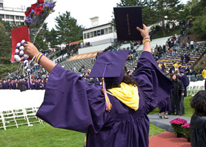 Photograph of a student in a graduation gown with arms in the air.