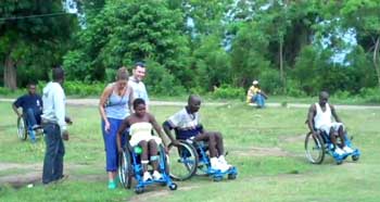 Photo of three spinal cord injury patients in Haiti testing out their new RoughRider wheelchairs on grassy terrain.