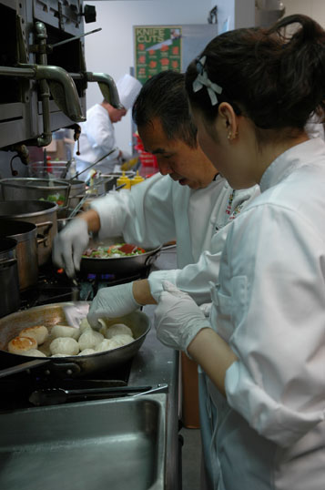 A photo of a chef helping a student in the kitchen.