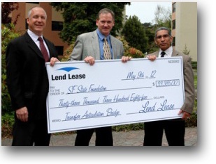 Photo of Bruce Berardi, senior vice president of Lend Lease, and Peter Read, vice president of Lend Lease, presenting a check to TAB Program Coordinator Paul Mendez.