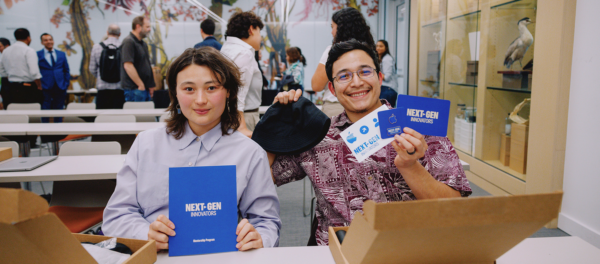 Two students smiling and holding Apple Next-Gen mentorship program booklets.