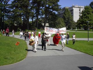 Two people carry the Multicultural AIDS Awareness Day banner, followed by the two lion dancers, and walk towards the Plaza