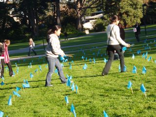 Two students inserting blue flags into the grassy Quad area