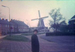 A still from the documentary, Robin's mother stands in front of a windmill in Munich as the Super-8 film home camera rolls.