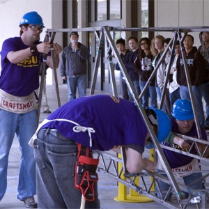Photo of engineering students assembling a steel bridge as other student look on.