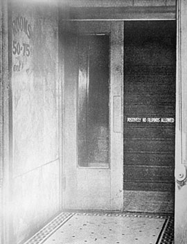 A 1930s black and white photograph of a sign outside a hotel that says 'Positively no Filipinos allowed.'