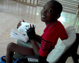 A photo of Vladimer, a teenage boy in Haiti, sitting in his wheelchair reading the chair's instruction manual